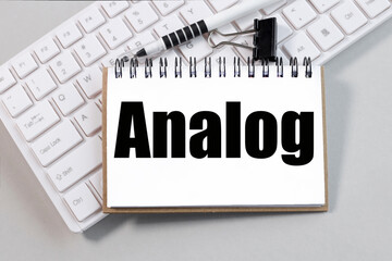 ANALOG word written on notebook. text on white paper on white keyboard