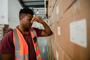 mixed race male worker stressing about retrenchment leaning against parcels in warehouse