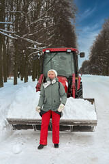 Portrait a woman in winter clothes against the background of a tractor with snow
