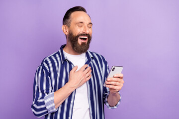 Photo of cheerful mature man look in smartphone read social media joke laugh isolated over purple color background