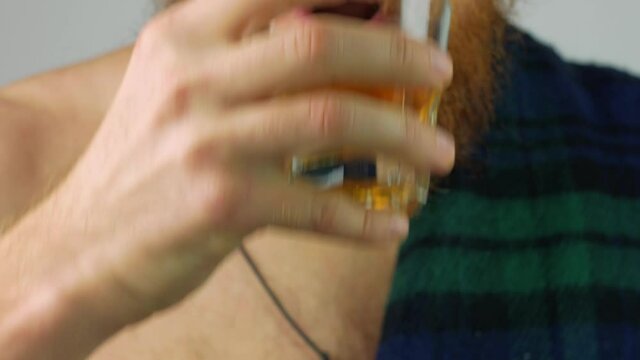 Irish bearded man in traditional green kilt celebrates St. Patrick's Day with scotch drink glass in hand. Scottish guy drinks whiskey in pub portrait.17 March cultural grand parade celebration Ireland