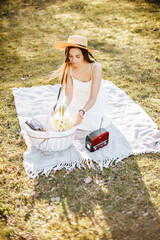 Obraz premium Girl with a straw hat in the spring in the park. Brunette with long hair sitting on a plaid on a background of summer nature. Youth and beauty.
