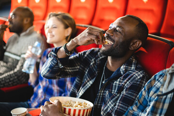 Friends are watching a movie in the cinema with popcorn. People sit in the armchairs of the cinema and look at the screen