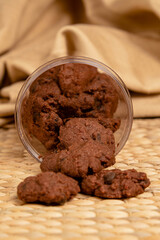 Delicious homemade chocolate cookies spilling out from containers on a bamboo mat