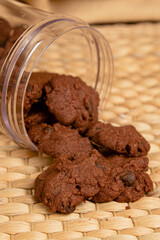 Delicious homemade chocolate cookies spilling out from containers on a bamboo mat