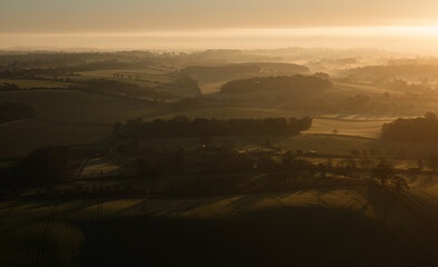 sunrise casts a golden glow on the rising mist filled Pewsey Vale from Martinsell Hill, Wiltshire