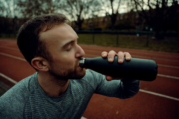 Caucasian male athlete standing on tracking field drinking watr from bottle 