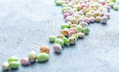 Candy, glazed chocolate Easter eggs sprinkled on a blue concrete textured background. Happy easter time. Dessert, sweets for joy, sweet-shop. Copy space, selective focus.