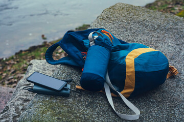 Fototapeta premium Smartphone is charged using a portable charger. Power Bank charges the phone outdoors with a backpack for tourism in nature.