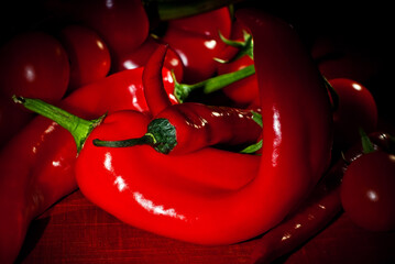 Chili peppers, bell peppers and tomatoes on a wooden board. Contrasting dramatic light as an artistic effect.