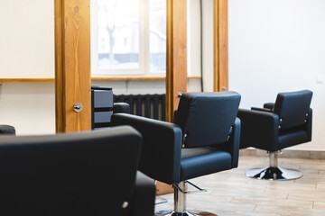 Beauty salon barbershop interior. Comfortable black leather armchairs in front of large panoramic mirrors in stylish wooden frames in a modern, cozy and bright room.