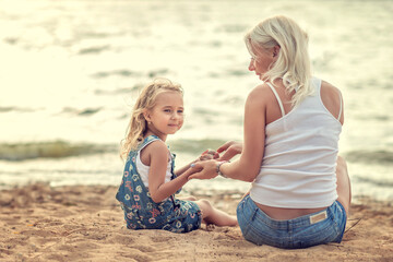 Fototapeta premium mom and daughter are sitting on the seashore. mom holds her daughter's hands