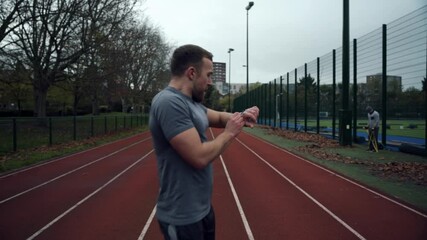 Caucasian male athlete running on tracking field checking watch