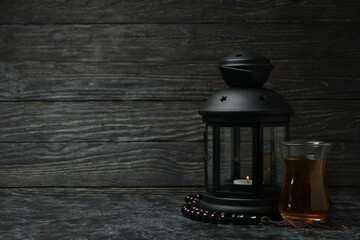 Obraz na płótnie Canvas Glass of tea, lantern and rosary against wooden background