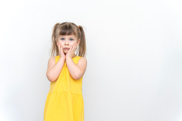 sad child girl in a yellow dress posing on a gray background, hands near the face