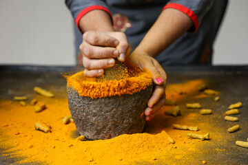 Woman hand powdering Indian spices turmeric powder splash explosion stone mortar Kerala India Sri...