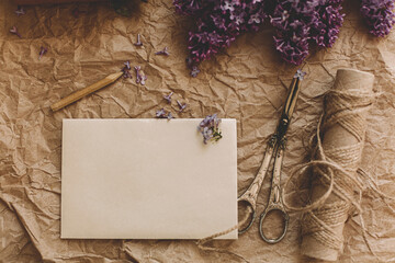 Stylish card, lilac flowers, vintage scissors, pencil, twine on rustic background, top view
