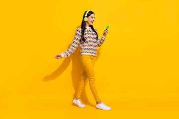 Fototapeta na wymiar Full size profile side photo of young beautiful happy excited girl in headphones go walk use phone isolated on yellow color background
