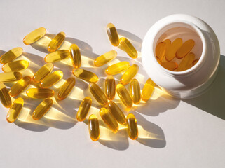 Pile of yellow capsules Omega 3, vitamin D, vitamin E, vitamin A, or fish oil on white background and in bottle. Cod liver, fish oil filled soft gel supplements for diet. Health care concept 