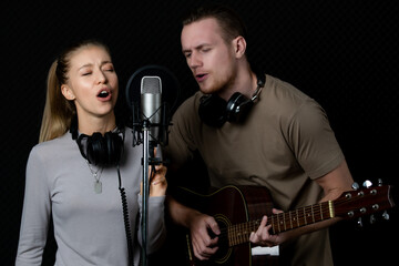 Young and beautiful and handsome male singers working together in voice recording studio with fun and happiness. Taken with studio light in dark style