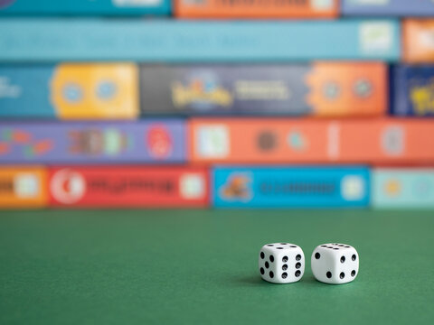 Two Dice On The Background Of Board Game Boxes. Dice Games For Kids, Tweens And Adults