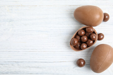 Whole and broken chocolate eggs with candies on white wooden table, flat lay. Space for text