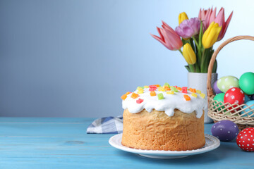 Obraz na płótnie Canvas Easter cake, colorful eggs and tulips on light blue wooden table, space for text