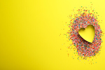 Heart shaped cookie cutter and sprinkles on yellow background, flat lay with space for text....