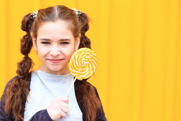 Girl with a big candy in her hands on a yellow background. Baby with yellow lollipop