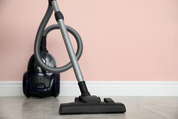 Modern vacuum cleaner near pink wall indoors, space for text