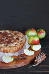 Traditional apple pie with spices on the brown wooden board. Apple pie decorated with sliced fresh apples and cinnamon sticks on the black background. Side view  with copy space