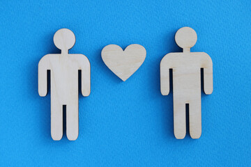 Wooden toy men and heart lying on blue background. Love between men concept