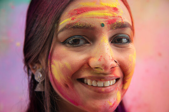 A YOUNG WOMAN WITH GULAL ON HER FACE LOOKING AT CAMERA AND SMILING	