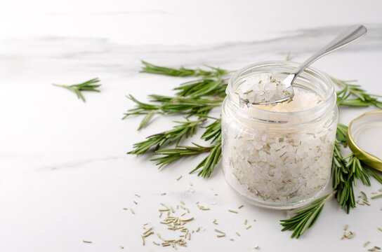 Glass jar of white sea salt and rosemary, fresh green rosemary on the white table.Empty space