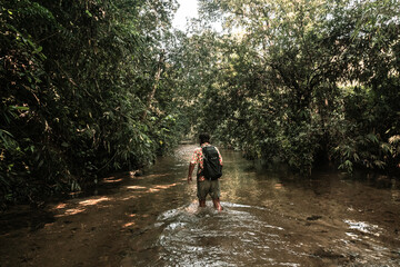 Podróżnik idący przez rzekę w dżungli, lesie tropikalnym.