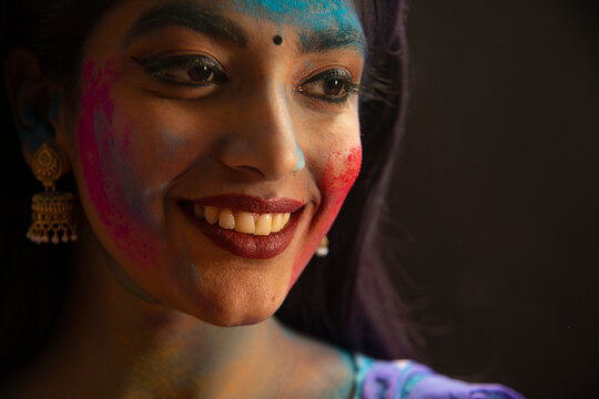 A HAPPY WOMAN WITH STREAKS OF COLOUR ON HER FACE LOOKING AWAY AND SMILING	