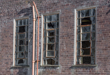 A close up of three broken old windows on a derelict abandoned building. All of the glass panes have been broken