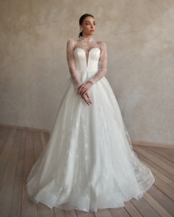 Fototapeta premium Full length portrait of young beautiful woman wearing white wedding dress. Elegant bride standing and posing against beige wall