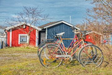 Fototapeta na wymiar Lone old bicycle forgotten in a rack in a holiday or vacation village with red and blue summerhouses (stuga). Red abandoned rusty bicycles provide an illustration of Scandinavian lifestyle and culture
