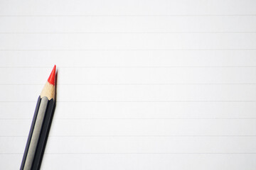 Sharpened wooden red color pencil with black body color on the notebook lined paper sheet background with copy text space