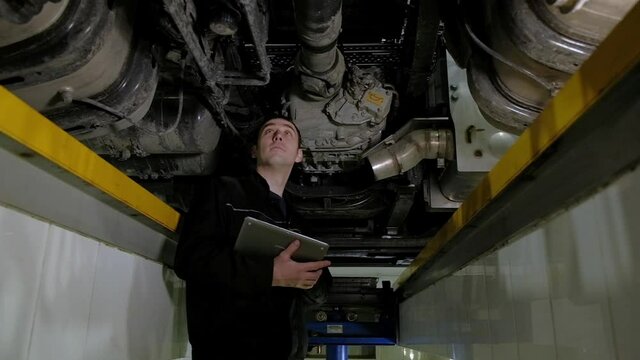 Auto mechanic makes an inspection of truck at service station. inspector records all breakdowns and problems with car in tablet. Auto service and repair cars. engineer works under car lifting machine