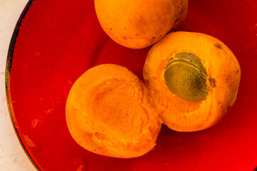 halves of a large fresh apricot on a red saucer, close-up