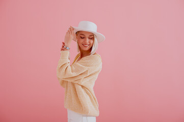 Happy smiling model wearing trendy yellow sweater, stylish silver wrist watch, white hat posing on pink background. Spring fashion conception. Copy, empty space for text

