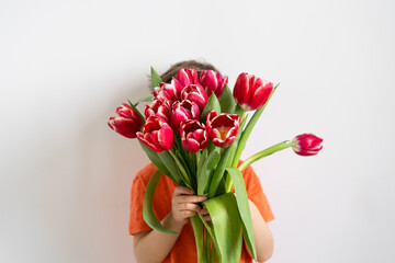 Cheerful happy child with tulips flower bouquet. Smiling little boy on white background.
