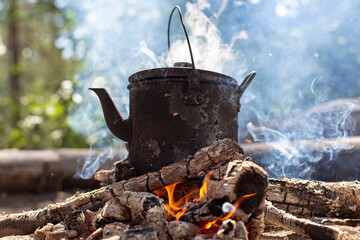 Boiling kettle with hot drink stands on a campfire in the smoke, in a forest.