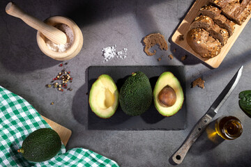 Flat lay composition with avocados on dark table with window shades.