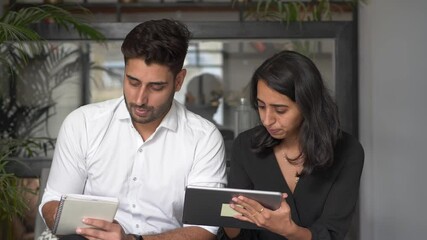 Two Professionals discussing project,showing details on tablet,writing notes,explaining and listening.Female Manager and Male Businessman Sitting in office Having Discussion and Working on the tablet.