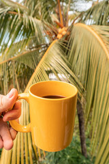 Poranna kawa w żółtym kubku na tle tropikalnej palmy.