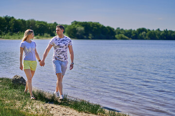 A young couple in love holds hands and walks along the lake.