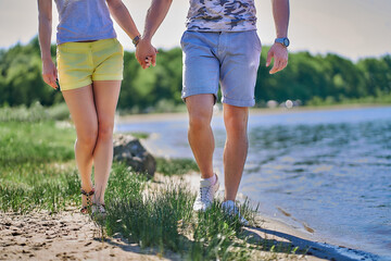 Young couple in love is walking on the beach and holding hands on a summer day. View of the legs below the waist.